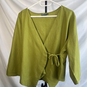 Front view of a green linen long-sleeve wrap top with a tie closure, hanging on a white hanger against a white background.