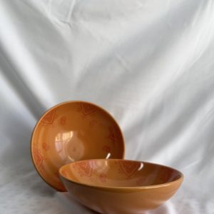 Two orange bowls, one upright and one tilted on its side, showcasing the full internal pattern against a white fabric.