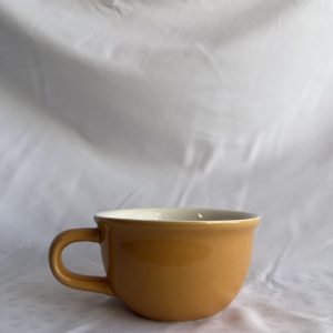 A glossy orange ceramic cup with a handle, seen from the front, sitting on a white crumpled fabric surface.